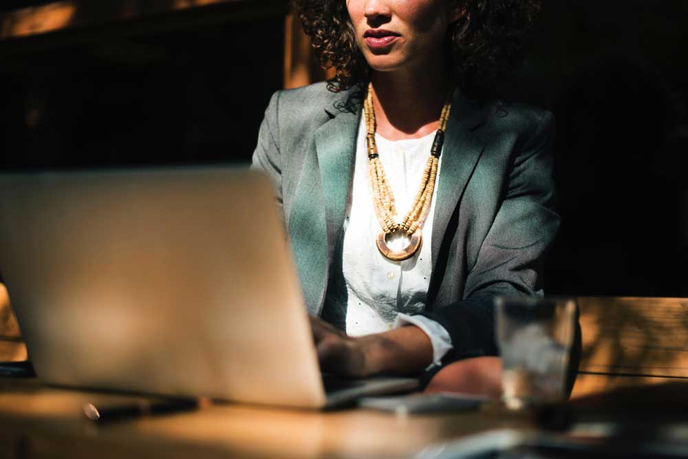 nose down view of woman wearing green blazer and beige necklace working on laptop