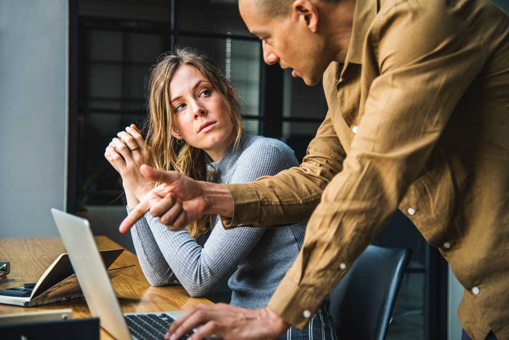 man in yellow shirt pointing at laptop while woman with blond hair is looking at him